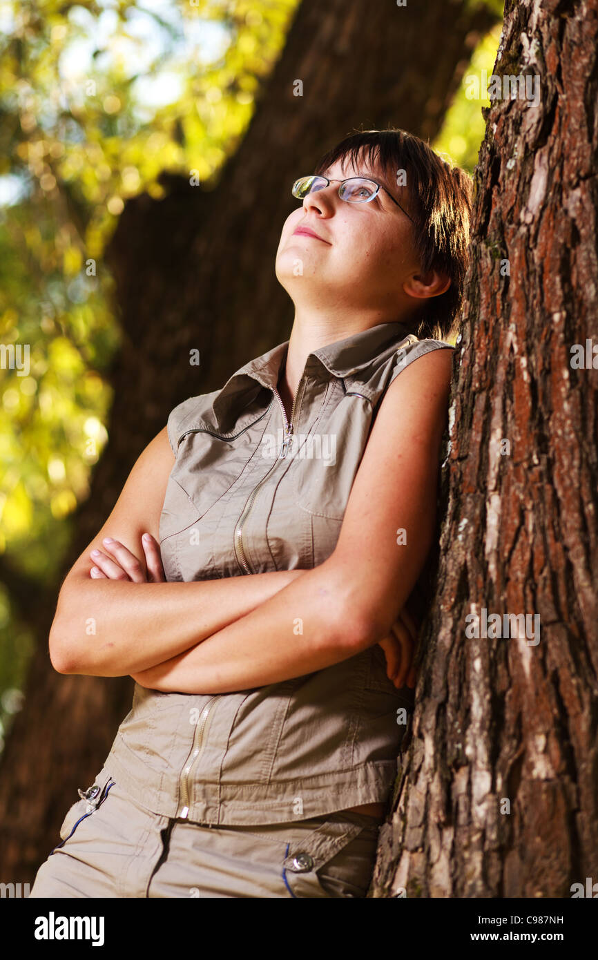 Portrait of dreamy girl in glasses near a tree. Stock Photo