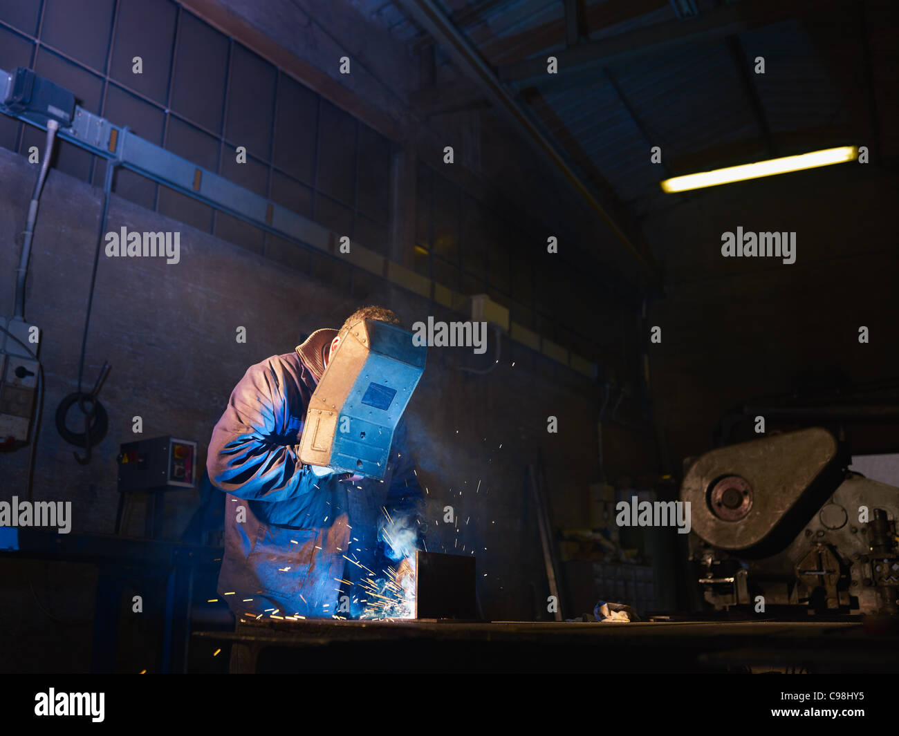Manual worker in steel factory using welding mask, tools and machinery on metal. Horizontal shape, side view, waist up Stock Photo