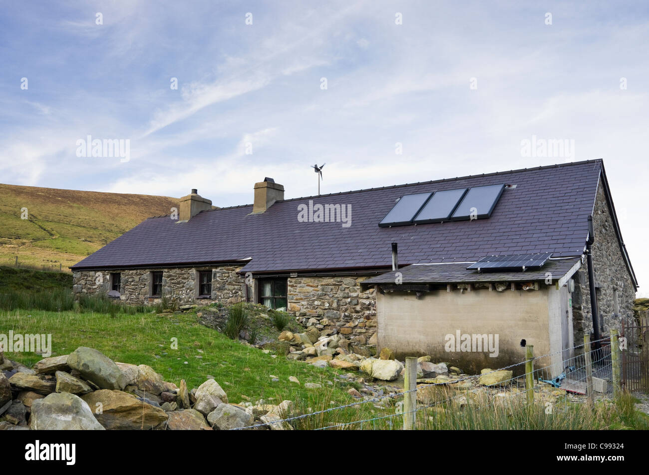 Remote rural cottage with solar panels on roof for heating hot water and generating electricity with small wind turbine spinning Stock Photo