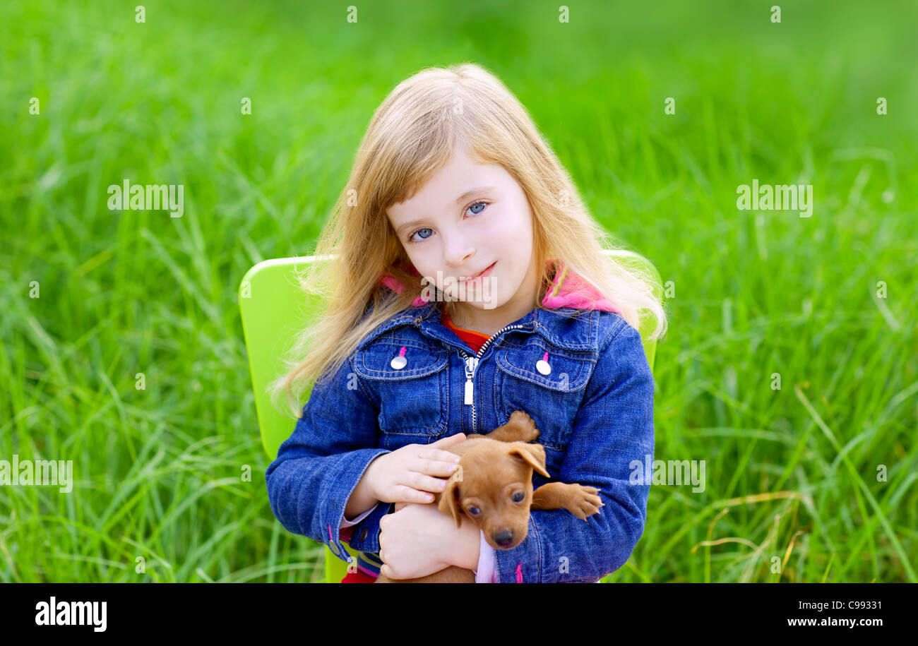 Blond kid girl with puppy pet dog sit in outdoor green grass Stock ...