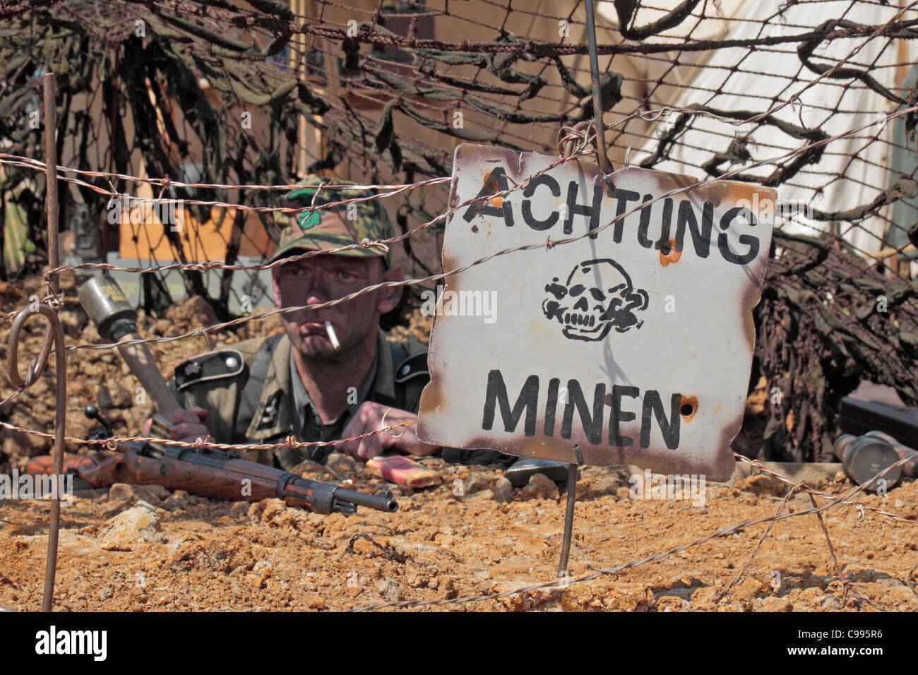 German soldier (re-enactor) behind barbed wire & an 'Achtung minen' sign at the 2011 War & Peace Show at Hop Farm, Kent, UK. Stock Photo