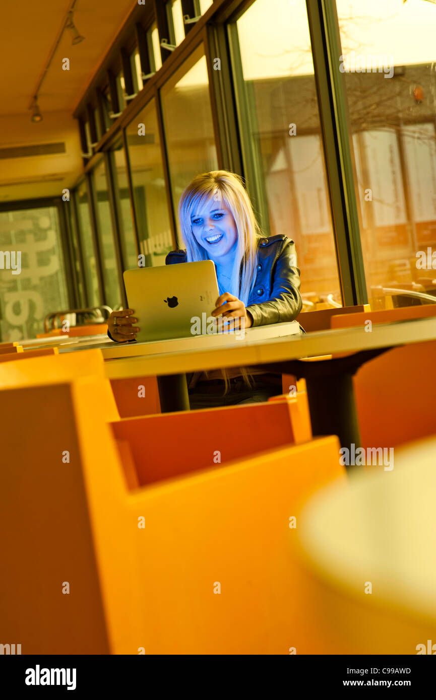 A 16 year old blonde haired slim teenage girl, using an Apple iPad, reading Facebook email laughing, UK Stock Photo