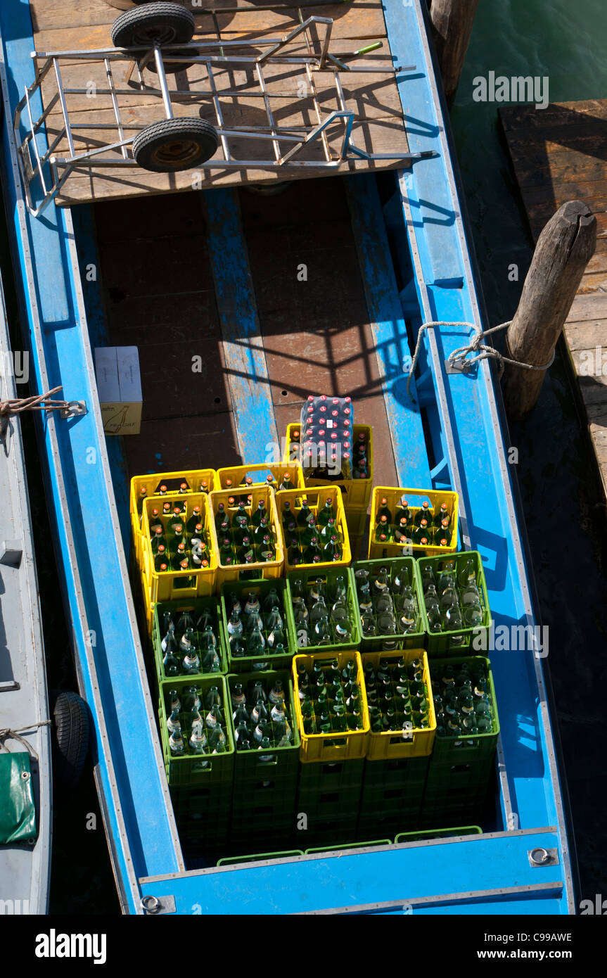Small blue boat laden with green and yellow crates of glass drinks bottles, some full and some empty, moored to a post Stock Photo
