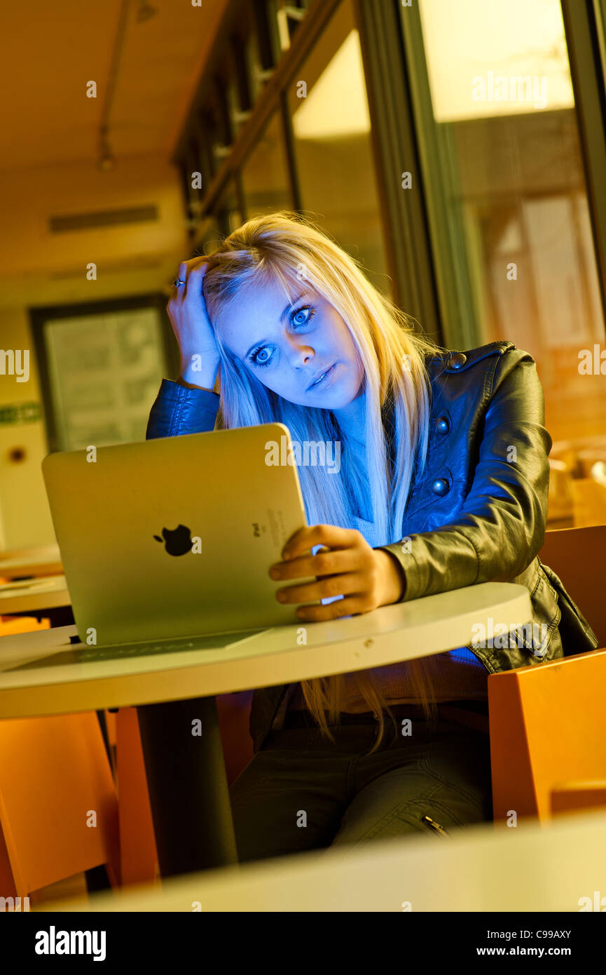 A 16 year old blonde haired slim teenage girl, using an Apple iPad, looking worried stressed anxious UK Stock Photo