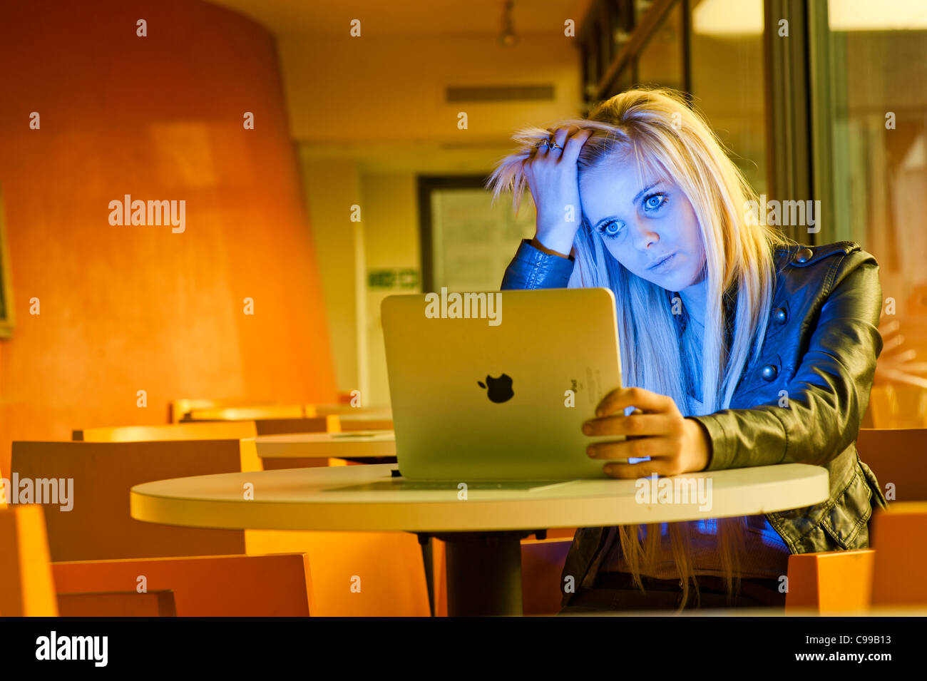 A 16 year old blonde haired slim teenage girl, using an Apple iPad, looking worried stressed anxious UK Stock Photo