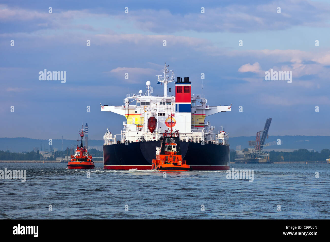 Maneuvers at sea on a cloudy day - Escorting tanker by tugs. Stock Photo