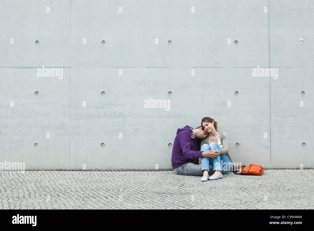 Germany, Berlin, Couple sitting in front of large wall on sidewalk Stock Photo