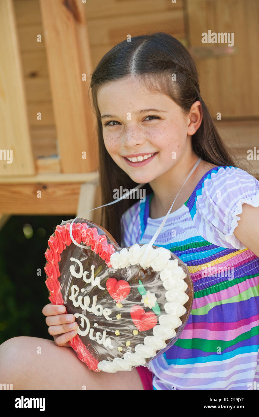 Germany, Bavaria, Girl with heart shape gingerbread, smiling, portrait ...
