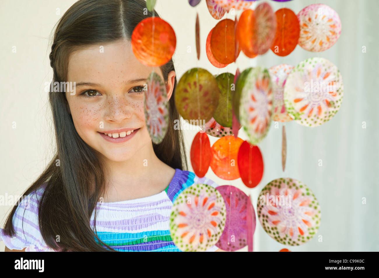 Germany, Bavaria, Girl with decorative sea shells wind chime, smiling, portrait Stock Photo