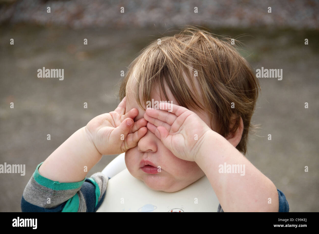 Very tired toddler rubs eyes outside after food Stock Photo
