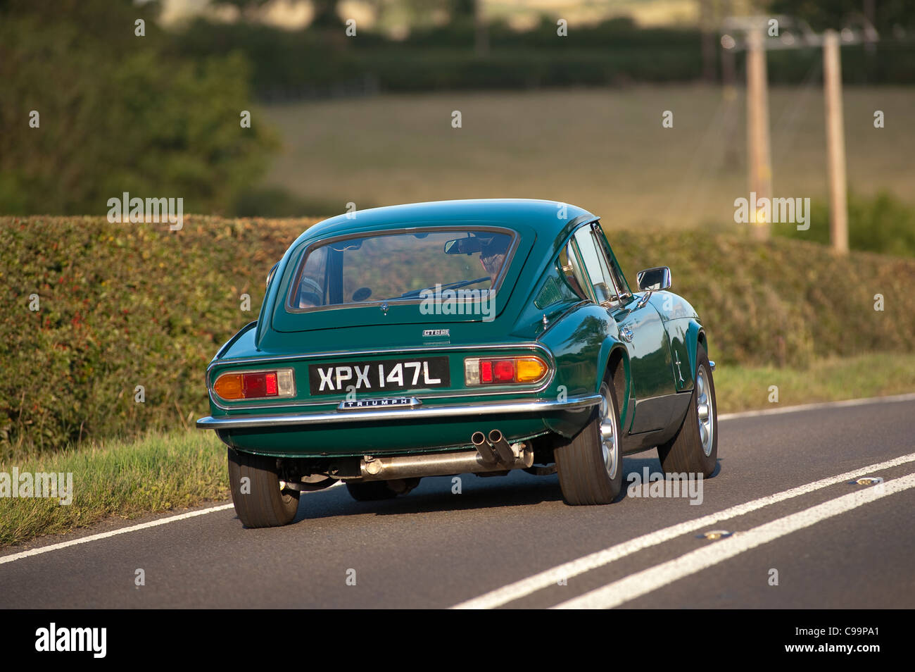 Rear view of a Triumph GT6 car being driven through rural England in the summertime. Stock Photo