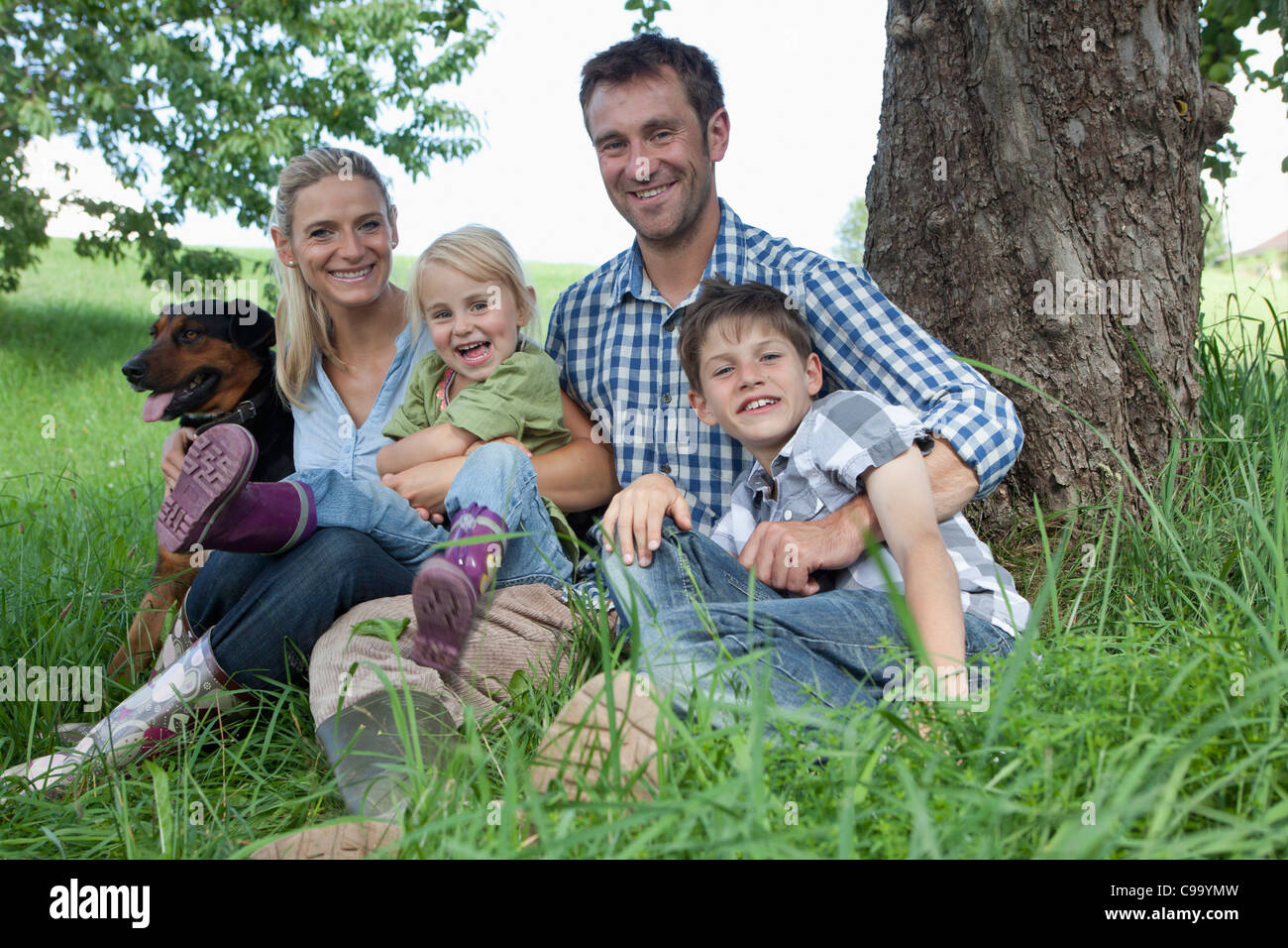 Germany, Bavaria, Altenthann, Family with dog under tree, smiling, portrait Stock Photo