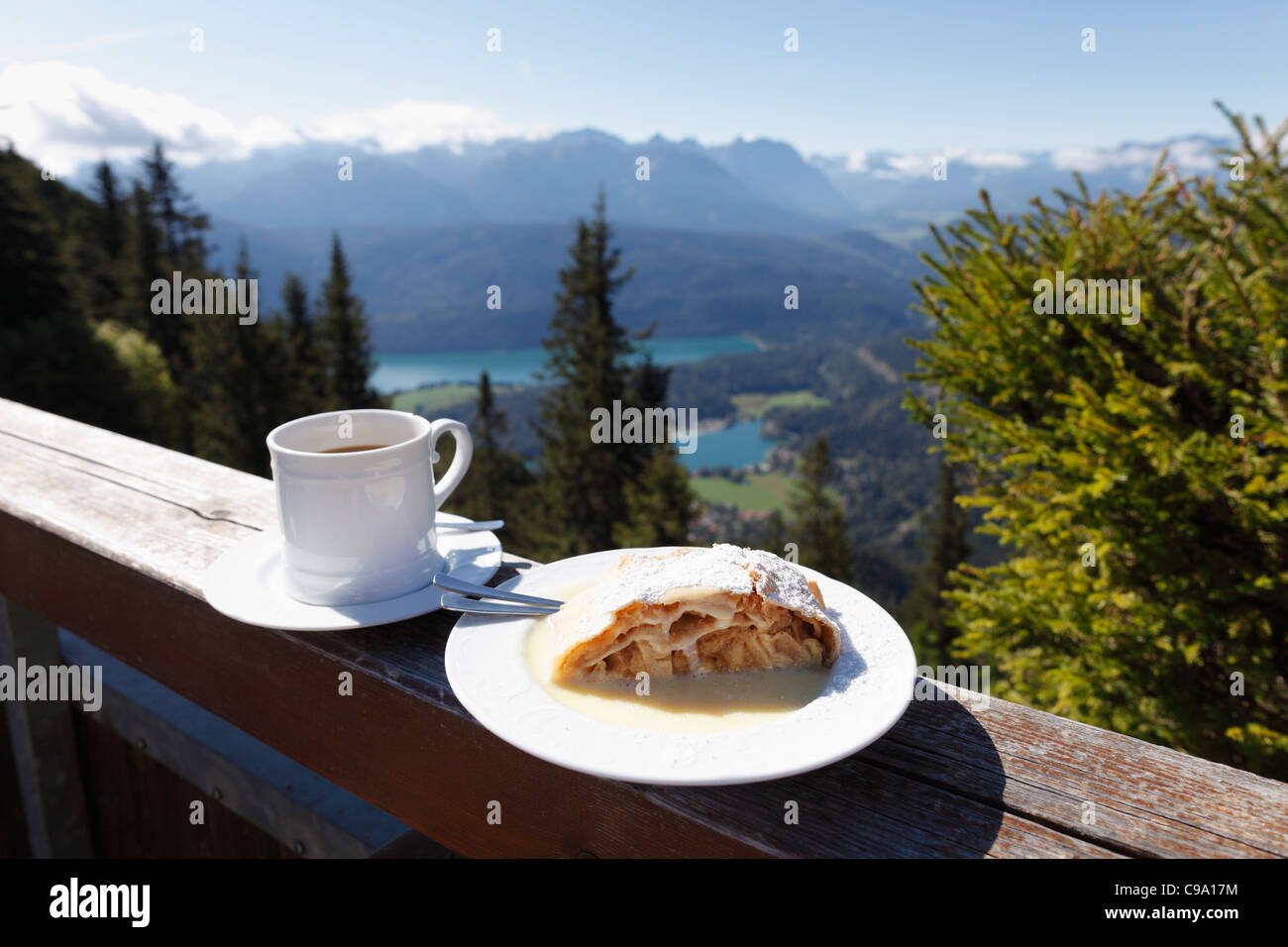 Germany, Bavaria, Upper Bavaria, Apple strudel and coffee cup on fence with mountains in background Stock Photo