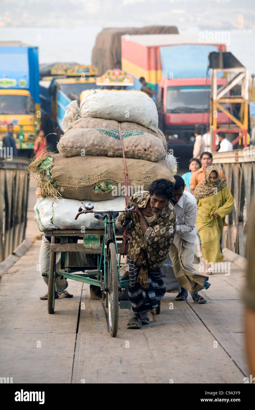 A rickshaw driver pulls his heavy load up the gangplank after disembarking from a ferry Chittaging Bangladesh Stock Photo