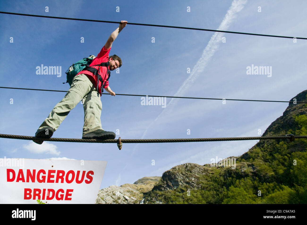 a climber crosses the rope bridge in glen Nevis at Steall Falls Stock
