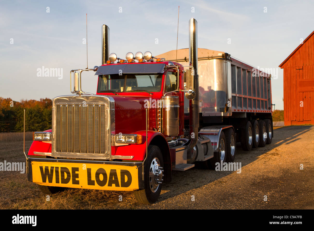 Tractor trailor with wide load sign is parked in front of a barn in the late afternoon sun. Stock Photo