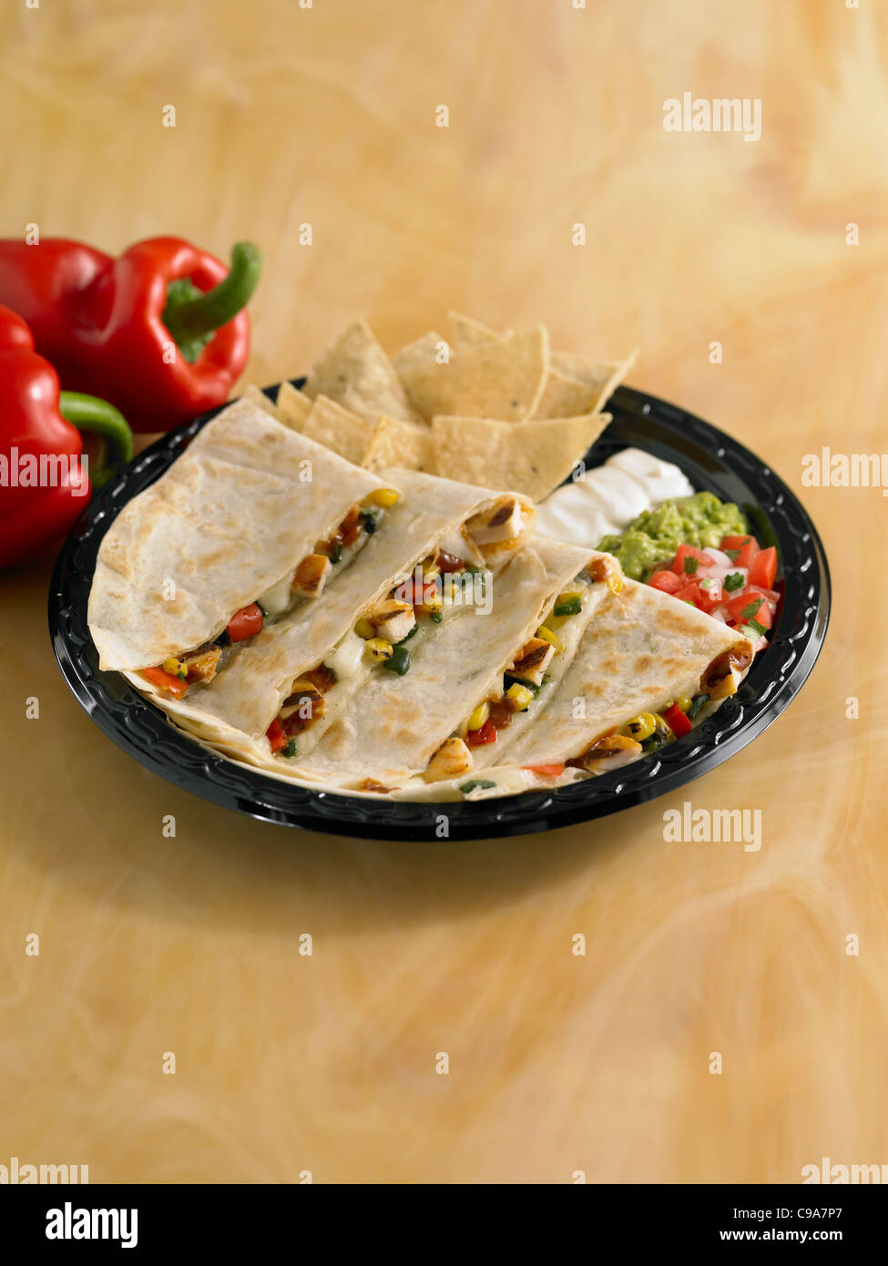 Grilled chicken and vegetable quesadilla served with sour cream, guacamole, salsa and chips Stock Photo