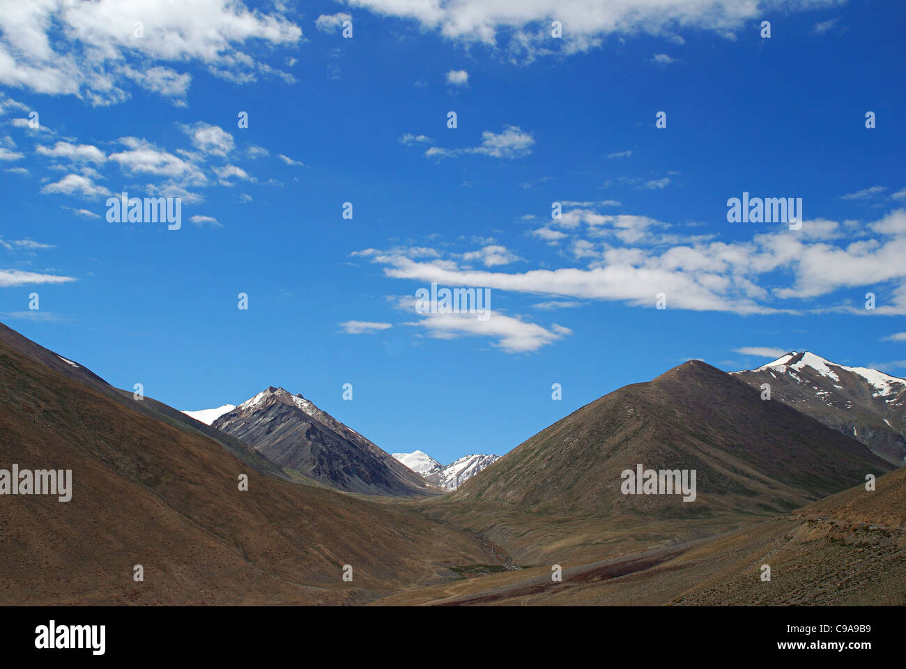 The truck on road to Leh, on the right hand bottom corner. Snow clad Himalayan Mountain Ranges, White clouds and Blue sky in the Stock Photo