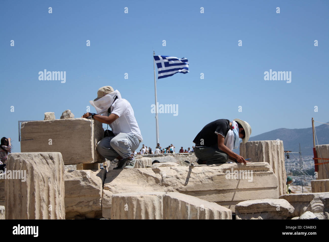Two archaeologists excavating the Acropolis, with the Greek flag in the middle at a distance. Stock Photo