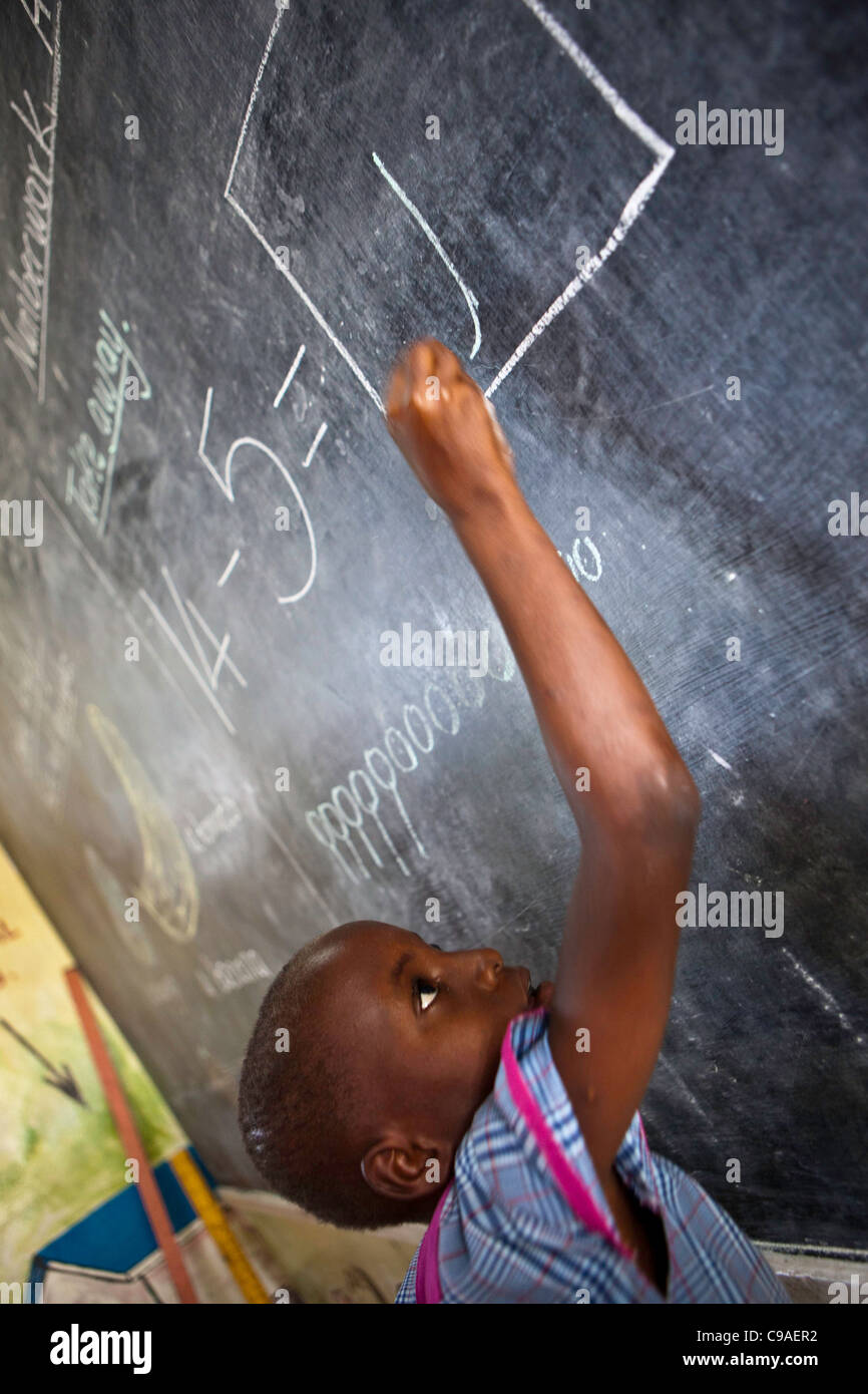 A child works out a maths question on the blackboard during a school class at the WEMA centre. Mombassa, Kenya. Stock Photo