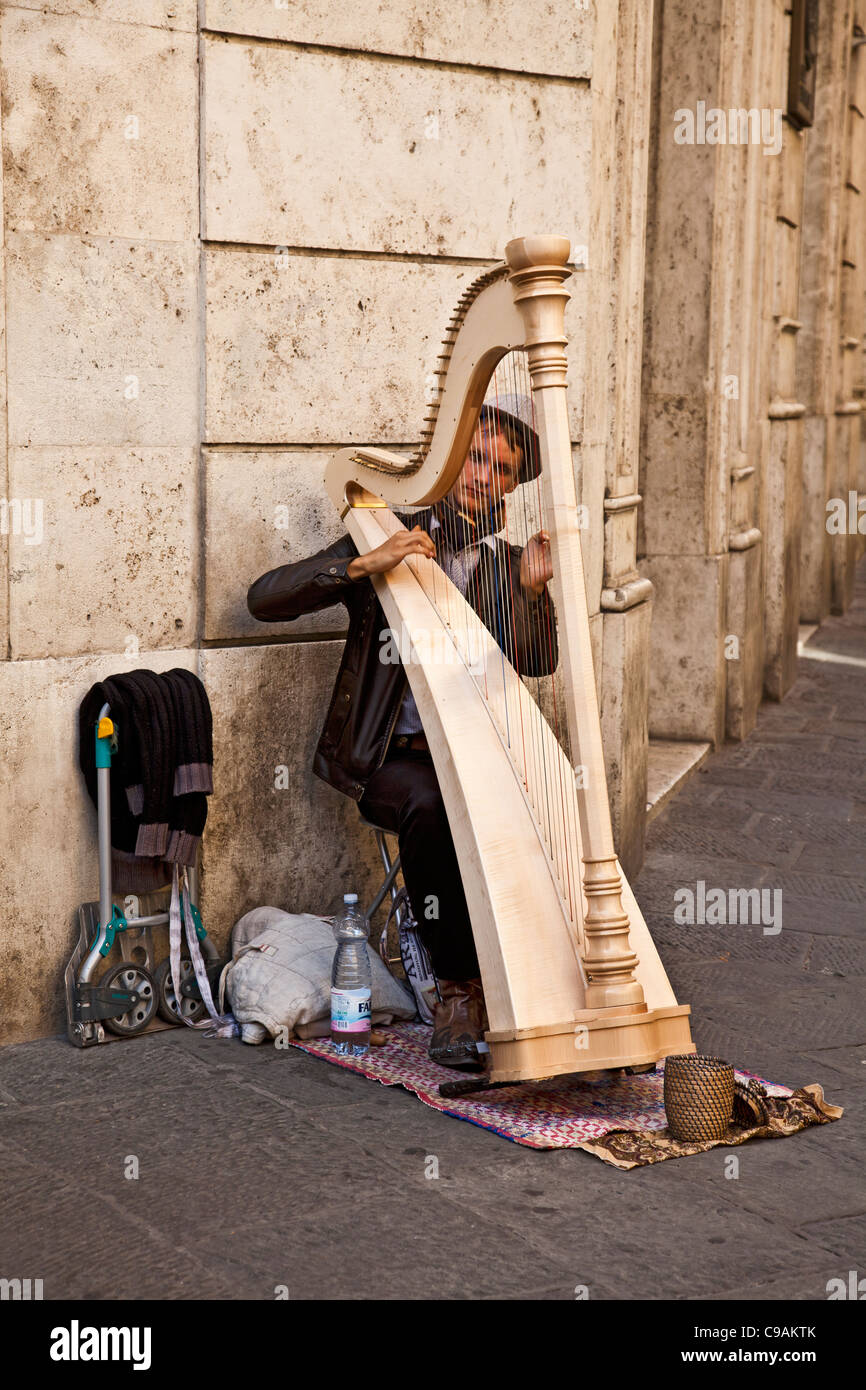 Young man harpist playing the harp in a street in the medieval city of Siena, Tuscany, Italy. Street entertainer/busker Stock Photo