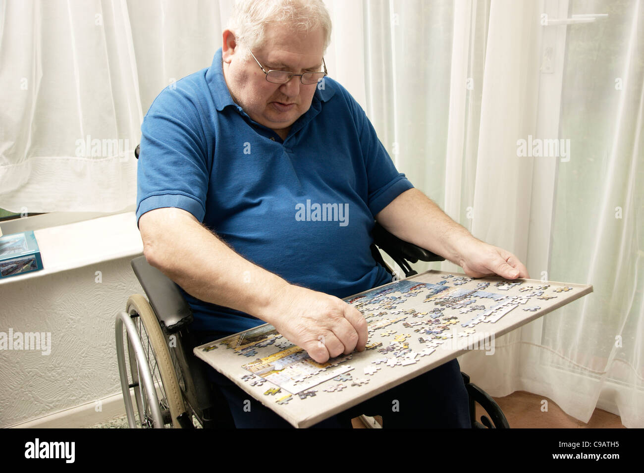 Disabled elderly man in a wheelchair doing a jigsaw puzzle to keep his