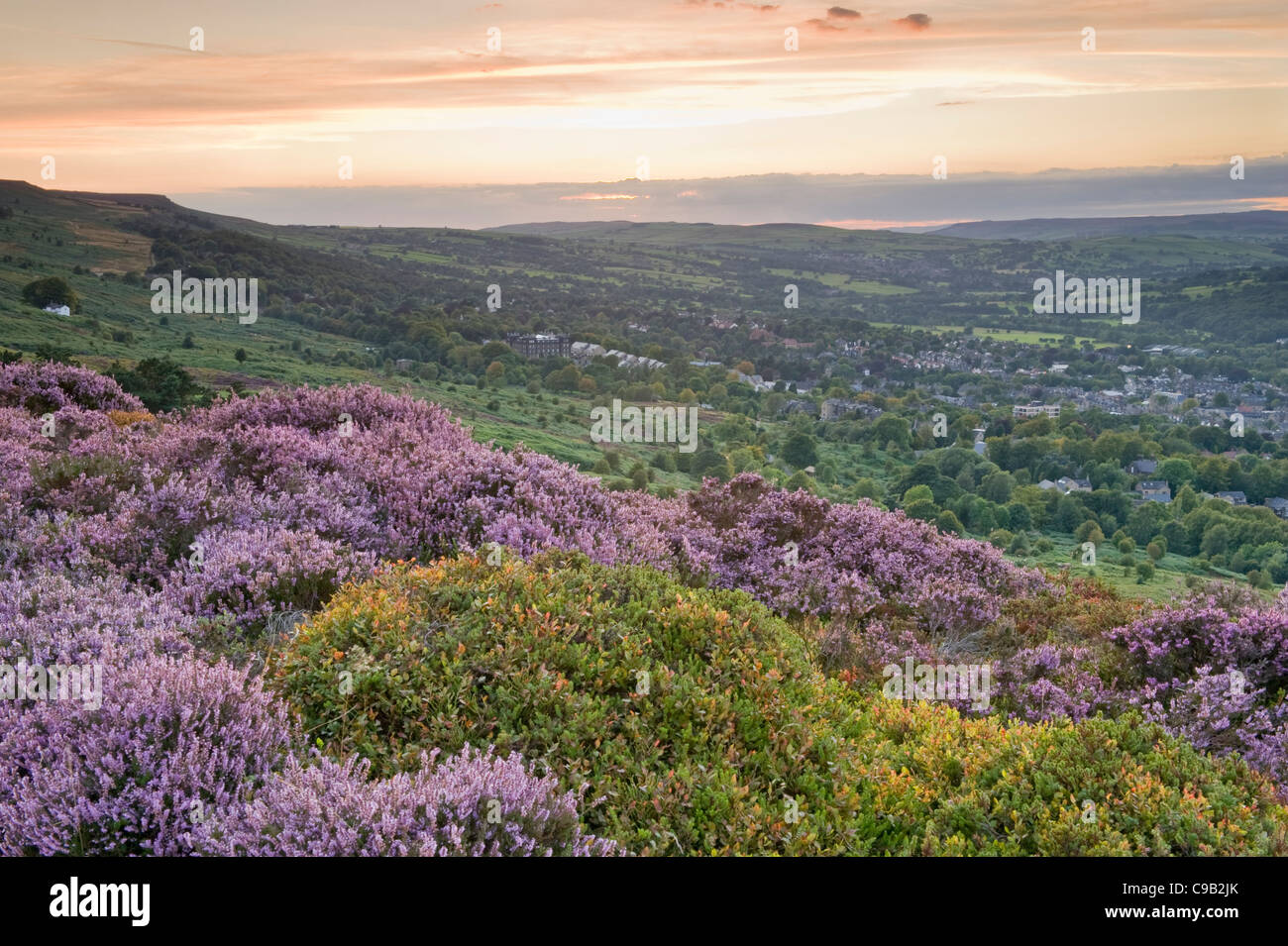 Orange sunset sky & high view across scenic Ilkley Moor (purple heather moorland) over town nestling in valley - Ilkley, Wharfedale, Yorkshire, GB, UK Stock Photo