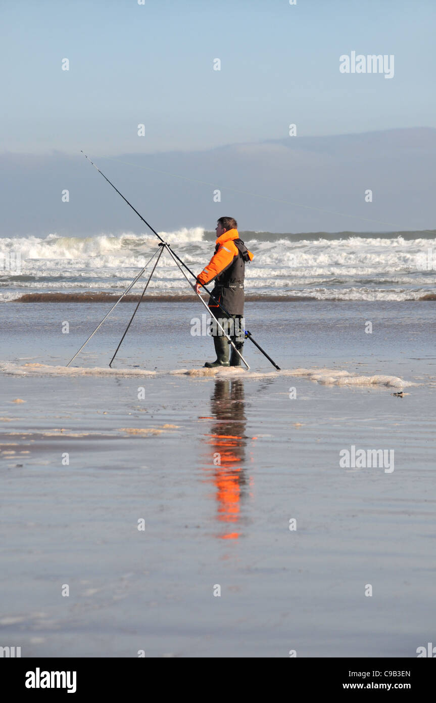 An angler stands patiently with his fishing rod and tripod on the Arbroath Beach in Angus. Stock Photo