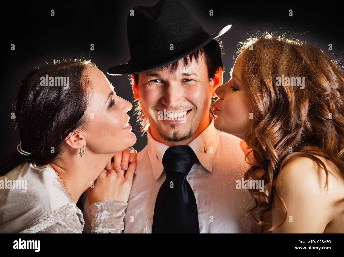 two pretty young women kissing smiling man from the sides Stock Photo
