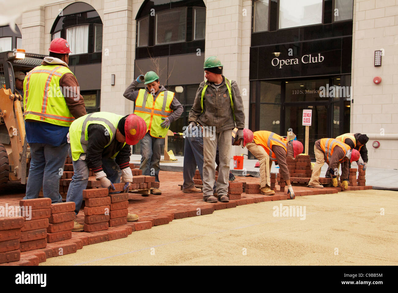 Construction workers lay paving bricks during Marion Street reconstruction project Stock Photo