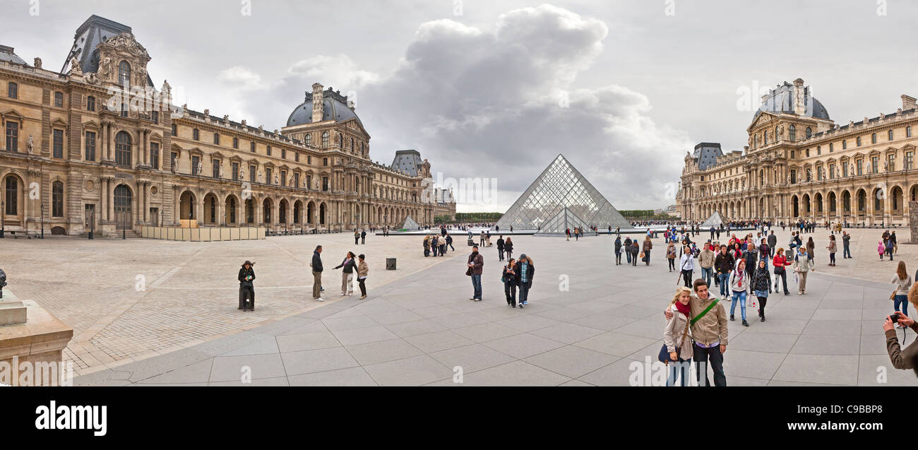 The Louvre Musée du Louvre central square courtyard with tourists, panorama showing the glass pyramid entrance Stock Photo