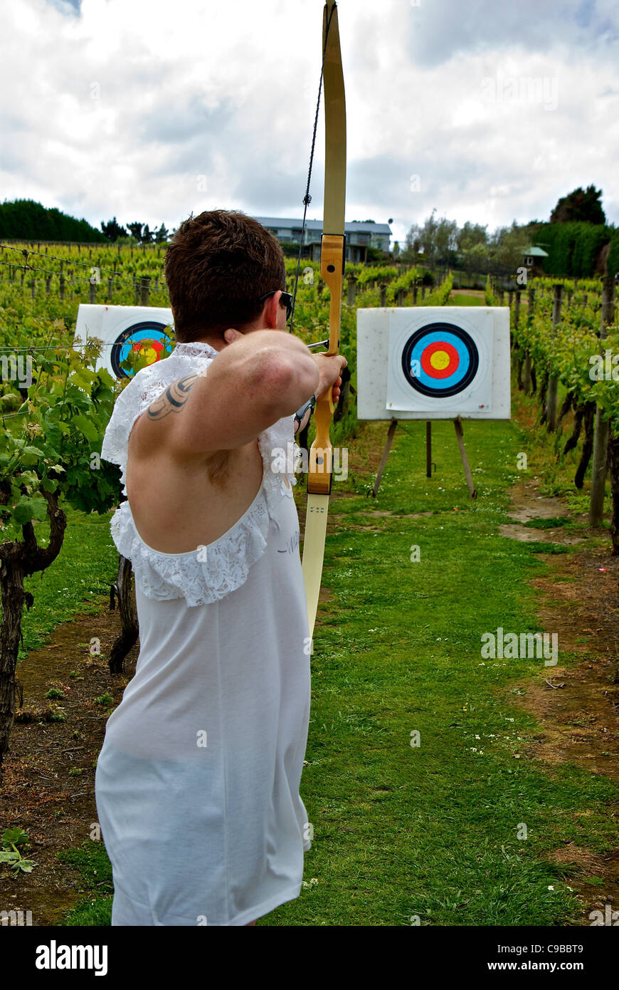 Bachelor party honoree in frilly slip trying archery at Wild on Waiheke vineyard Stock Photo
