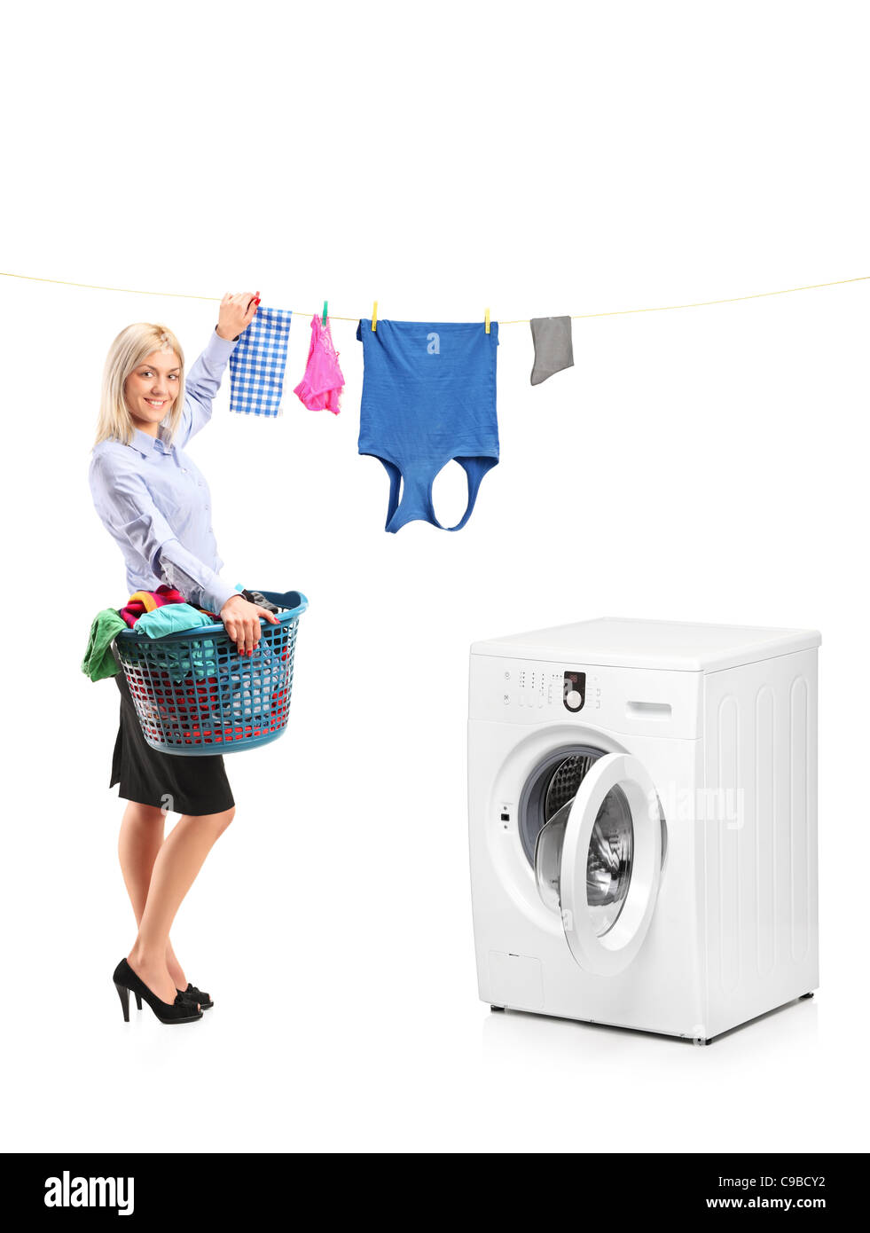 Young smiling woman hanging clothes on clothes line next to a washing machine Stock Photo