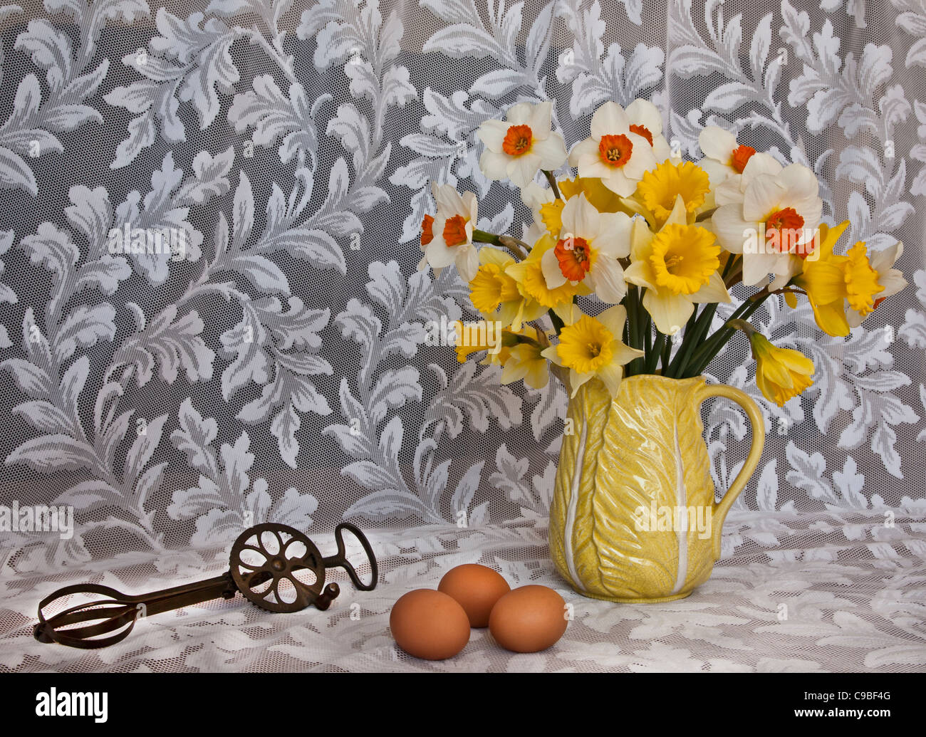 Still life spring Daffodil flowers in vase, vintage pitcher, pots,antique eggbeater cooking utensil, 3 brown eggs, white lace Colourful baking tools Stock Photo
