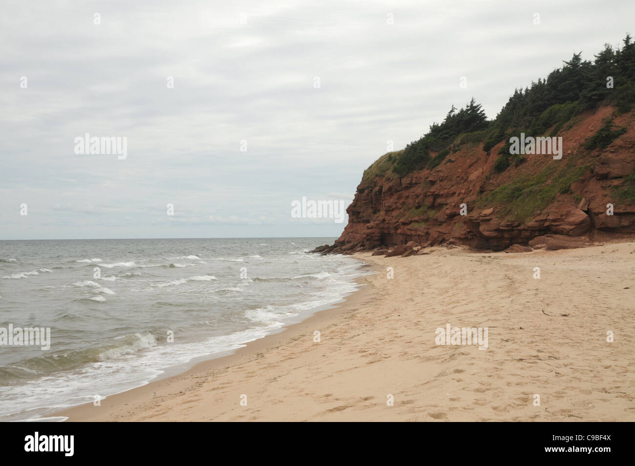 As red cliffs create the background, waves break on the Red Point beach on Prince Edward Island, Canada. Stock Photo