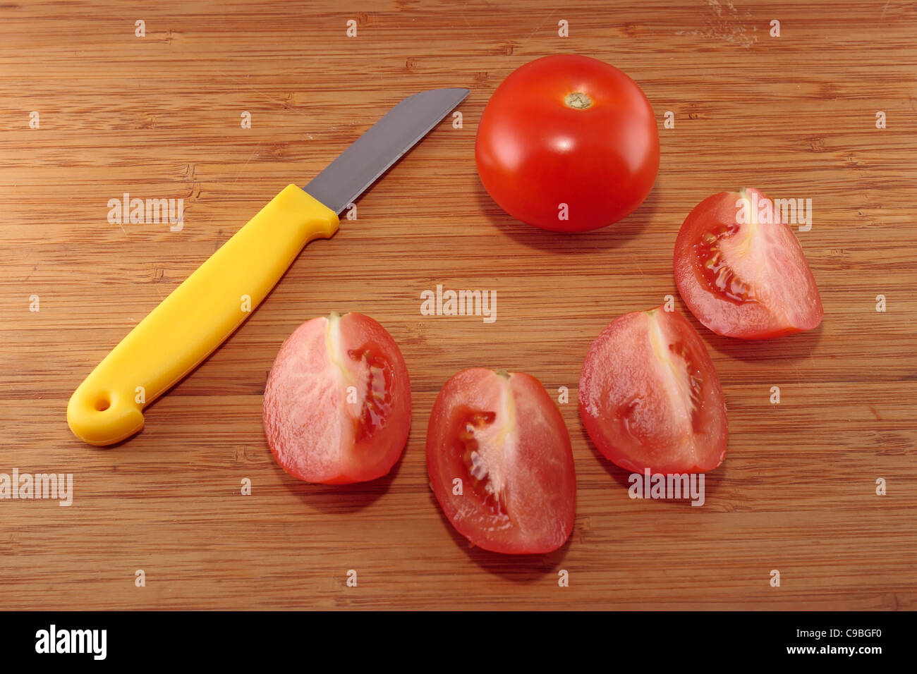 Tomato and four tomato quarters on a chopping board Stock Photo