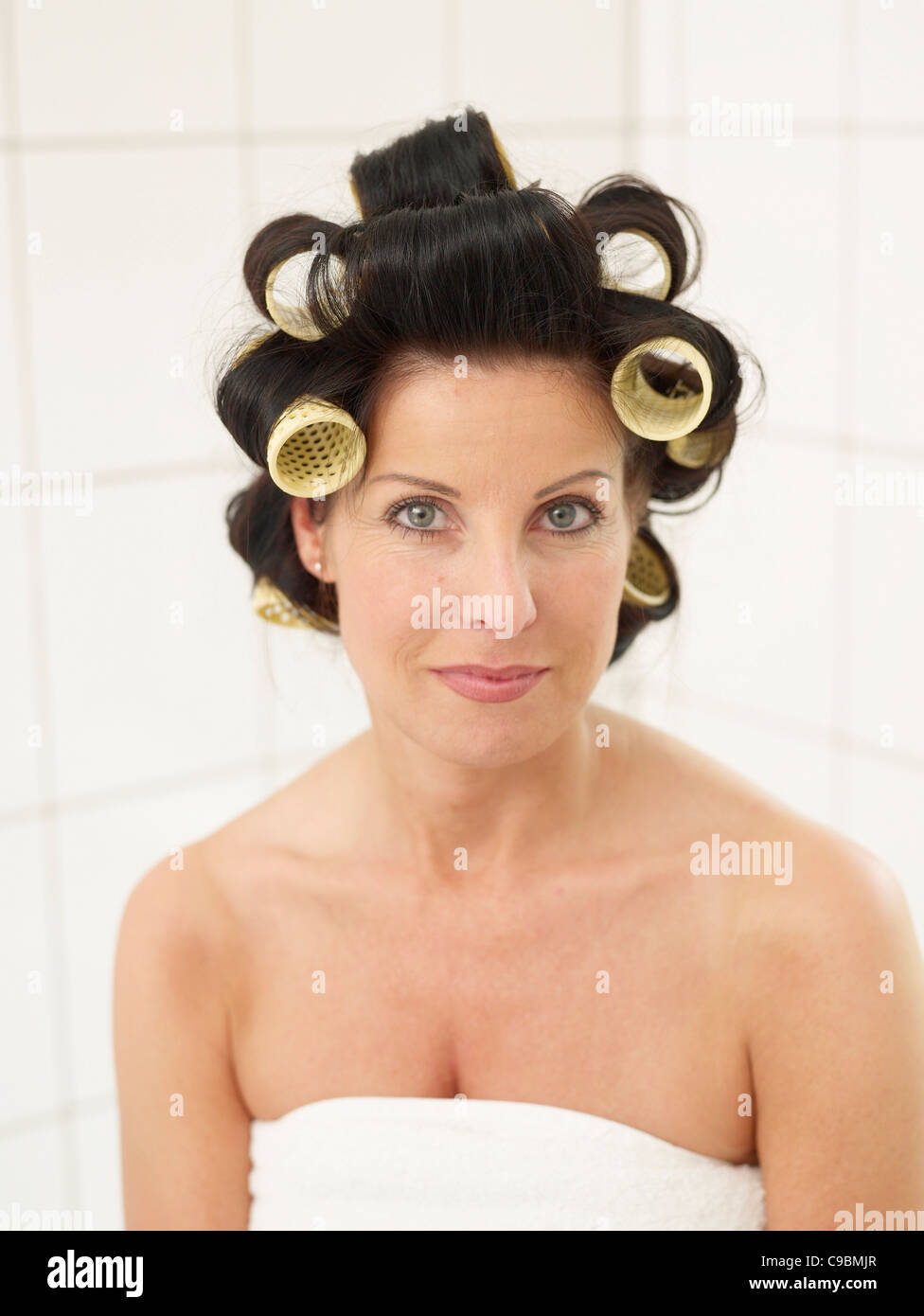 Mature woman in towel with hair rollers, smiling, portrait Stock Photo