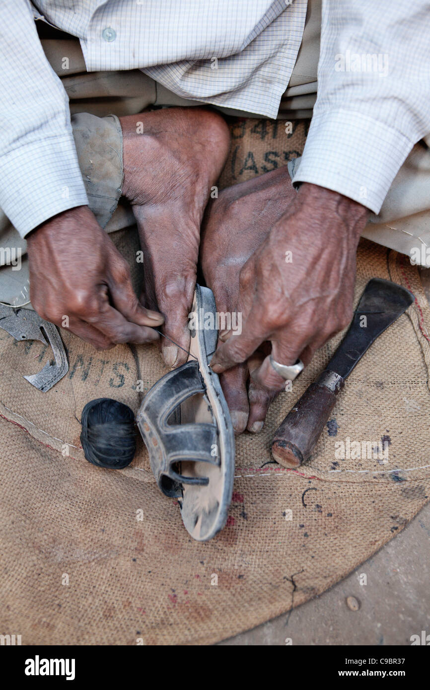 Man repairing shoes on street in village of Sarod, Gujarat state, India