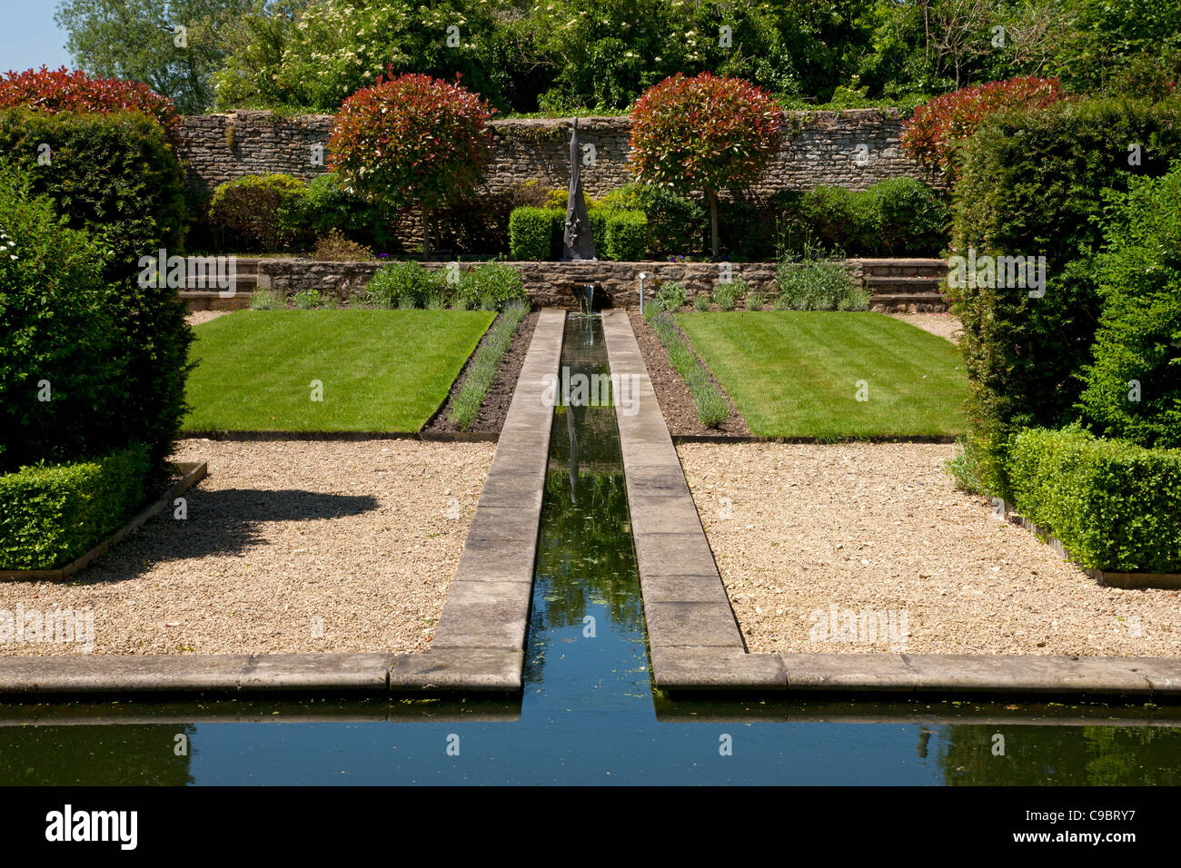 Rill water feature edged with lavender in walled private garden laid out in a formal style with obelisk as focal point, England. Stock Photo