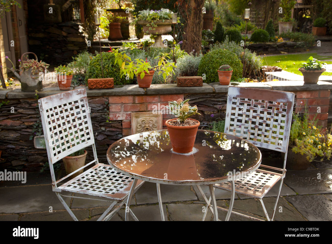 Metal table and chairs on stone patio in english autumn garden Stock Photo