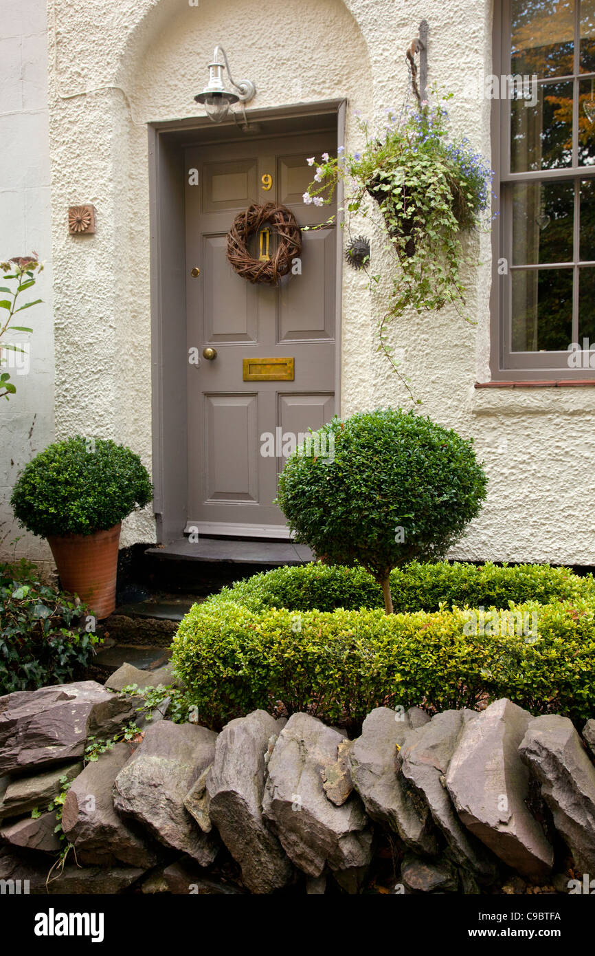 Front entrance to an English cottage,with dry slate wall ,topiary ,hanging basket , wooden door and sash window,england. Stock Photo