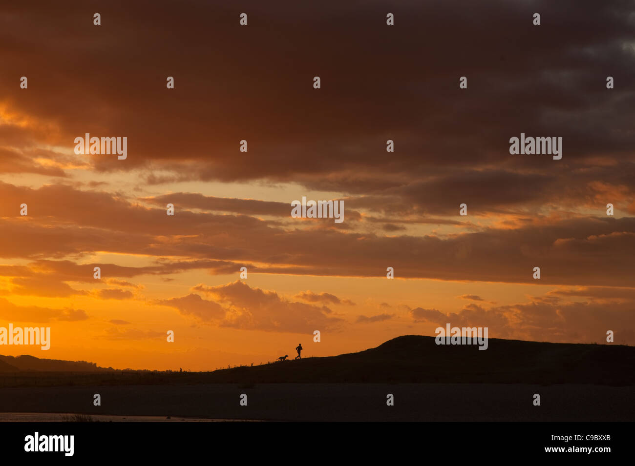 Dog walker at sunset Cley Beach UK October Stock Photo