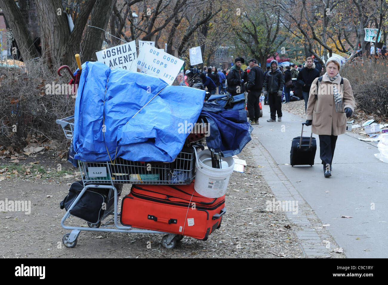 November 21, 2011, an unidentified woman passes by a shopping cart loaded with the belongings of a protester vacating St. James Park following the decision handed down this morning's by Ontario Superior Court judge David Brown, upholding the Occupy Toronto tent camp eviction. Stock Photo