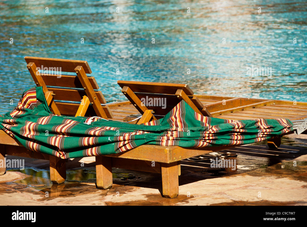 Two wooden chaise lounges with green towels beside swimming pool Stock