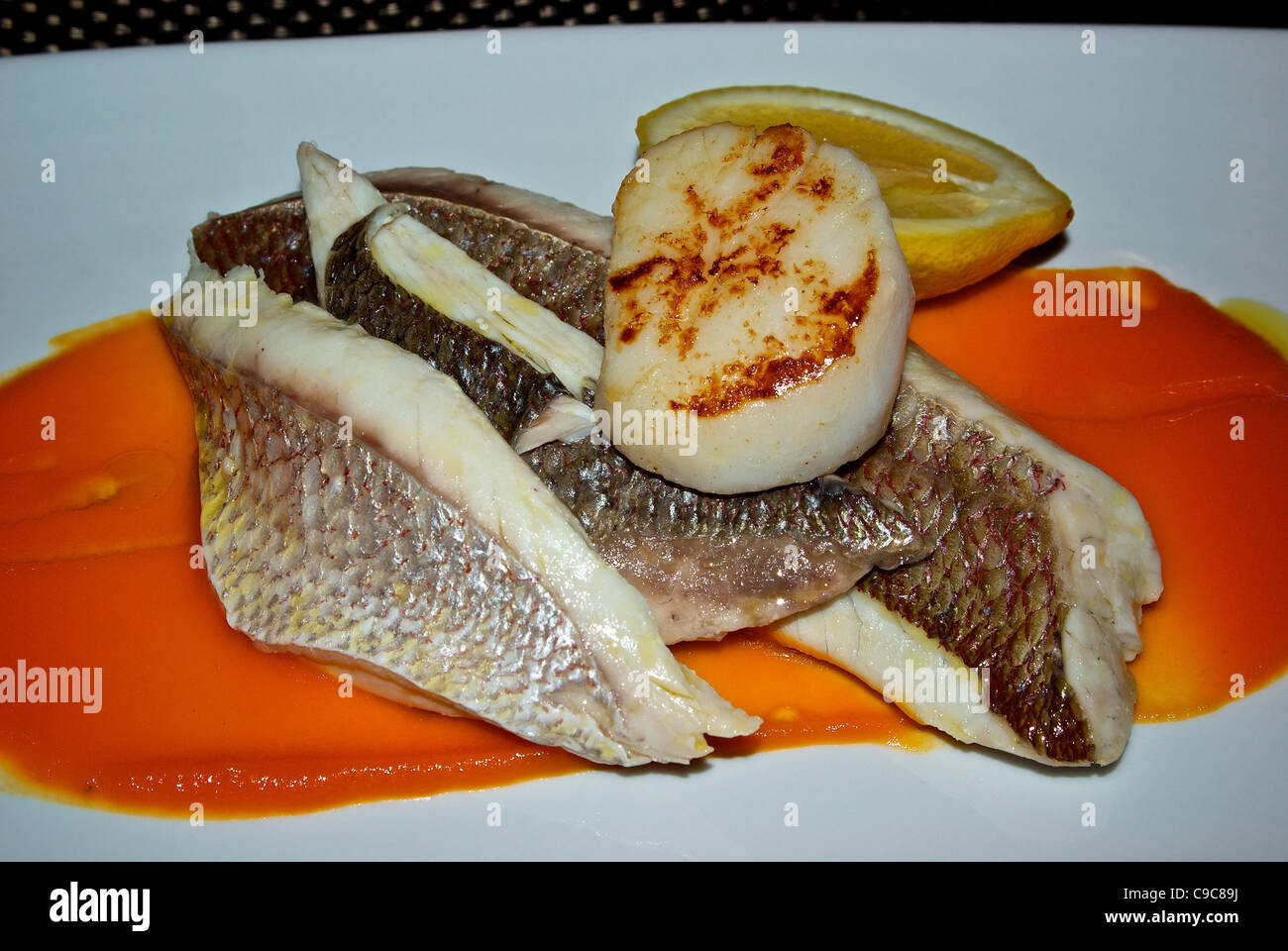 Steamed snapper fish filet caramelised seared scallop on carrot puree with half lemon seafood main course Stock Photo