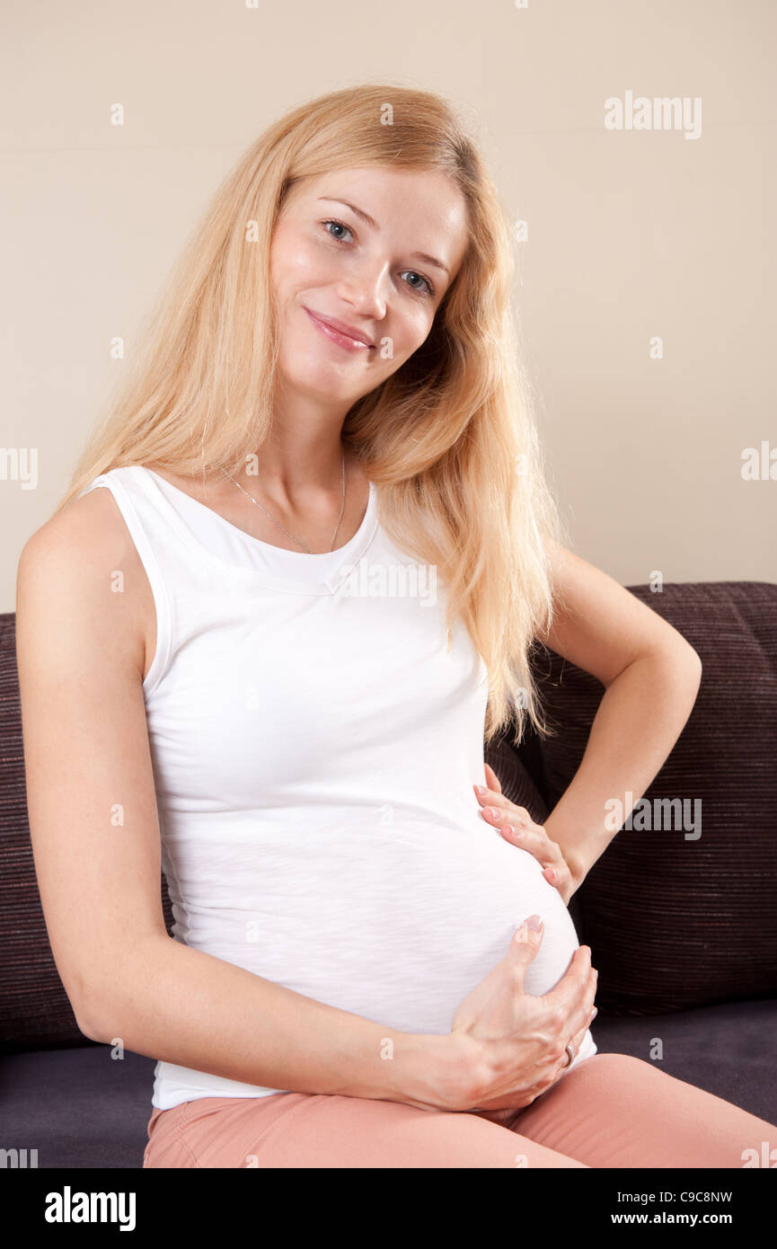 Young Pregnant Blonde Woman Sitting On The Couch And Smiling Stock