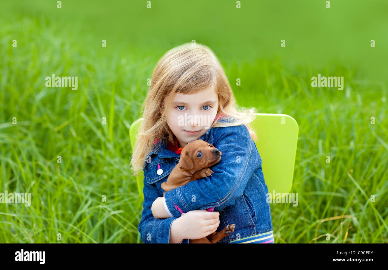 Blond kid girl with puppy pet dog sit in outdoor green grass Stock ...
