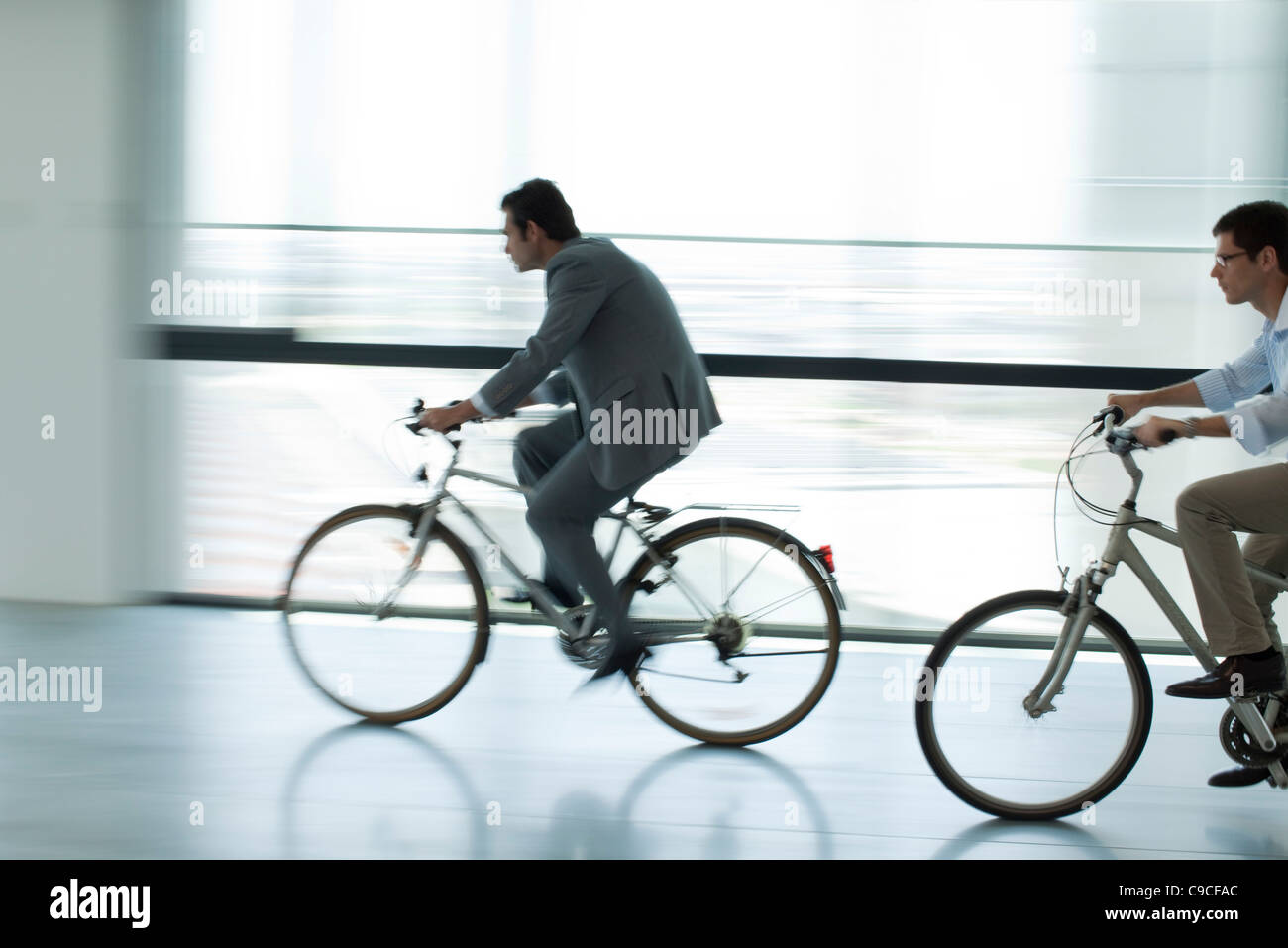 Businessmen riding bicycles indoors, silhouette, blurred motion Stock Photo