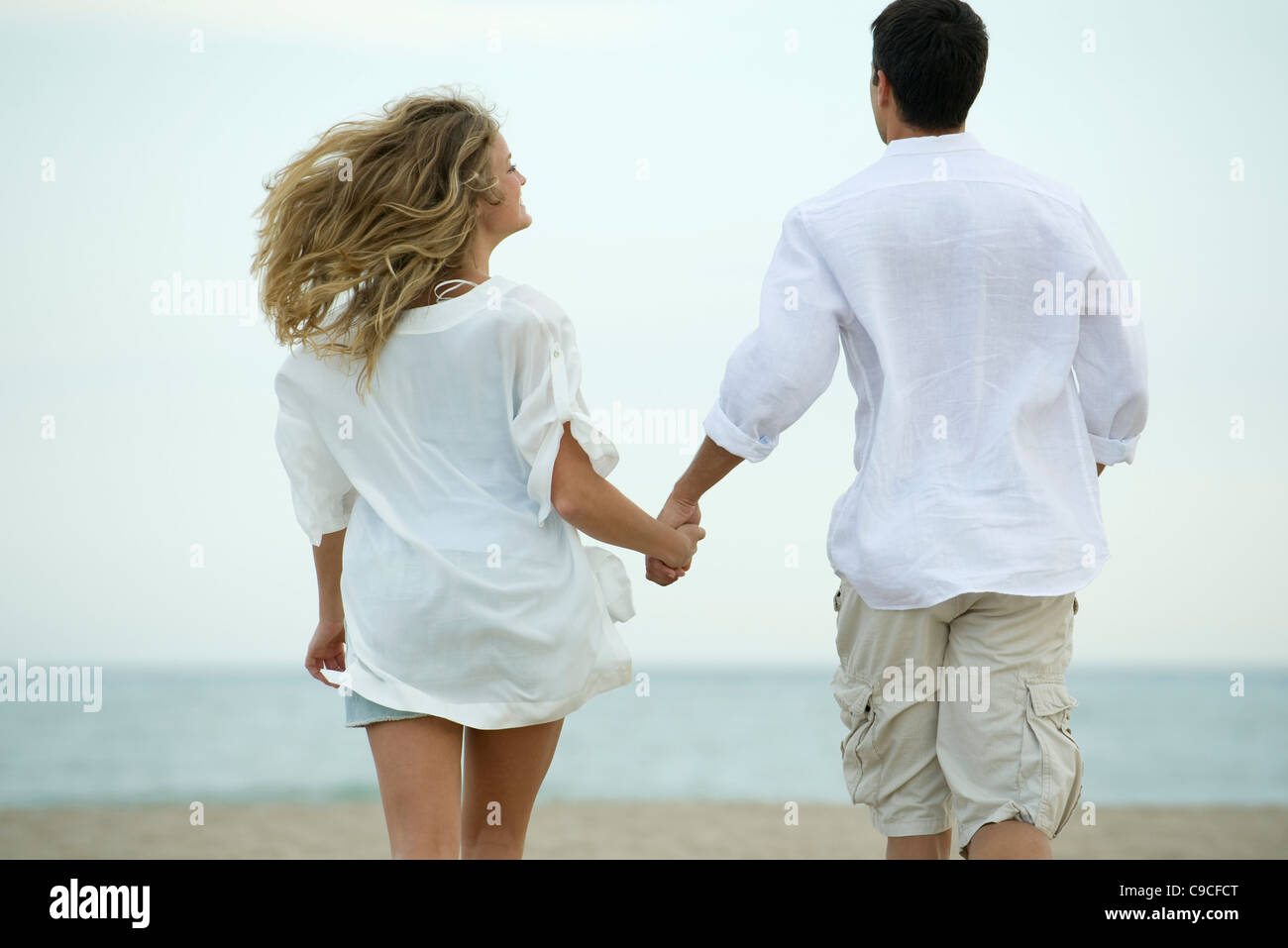 Couple walking hand in hand at the beach, rear view Stock Photo - Alamy