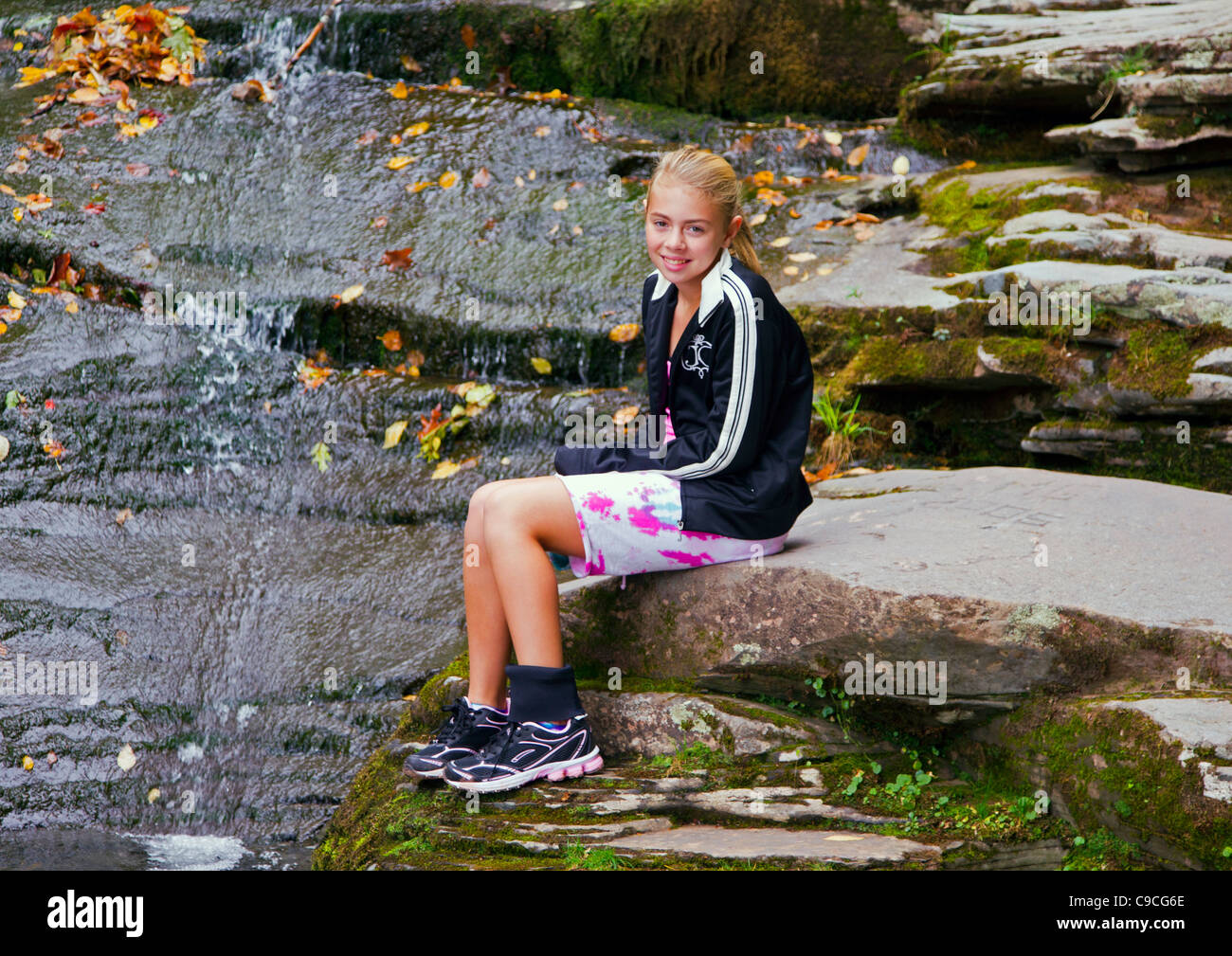 A young girl sitting on a rock near a waterfall Stock Photo